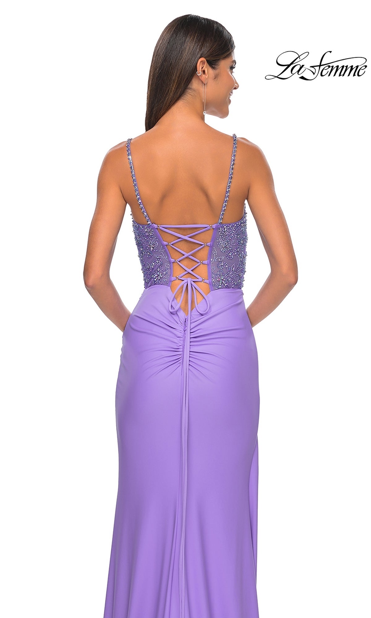 A woman wearing the La Femme Beaded-Corset Long Prom Dress 32089, a sleeveless lavender gown with a beaded lace-up back and ruched details.